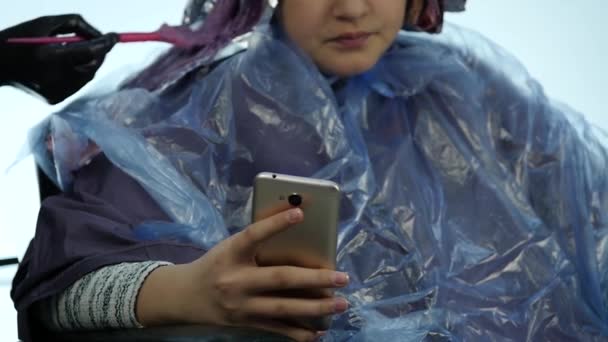 Chica hablando por teléfono mientras que la peluquería hace peinado, tinte para un adolescente en un salón de belleza. cámara lenta — Vídeos de Stock