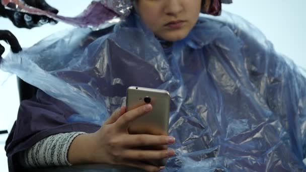 Dziewczyna rozmawia przez telefon podczas fryzjera sprawia, że fryzurę, farbowania dla nastolatek w salonie kosmetycznym. zwolnionym tempie — Wideo stockowe