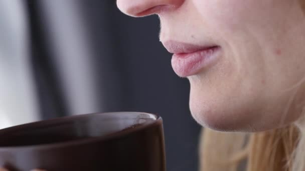 Mujer joven y pensativa bebe café o té cerca de la ventana. 4K — Vídeos de Stock