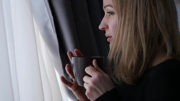 Ung kvinna dricker kaffe eller te nära fönstret. slowmotion — Stockvideo