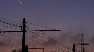 Yüksek gerilim elektrik Kulesi, siyah duman fabrika ve akşam gökyüzünde uçakta izi. 4k