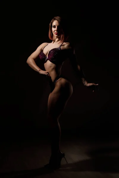 beautiful fitness woman, muscular girl poses on dark background. female body-building