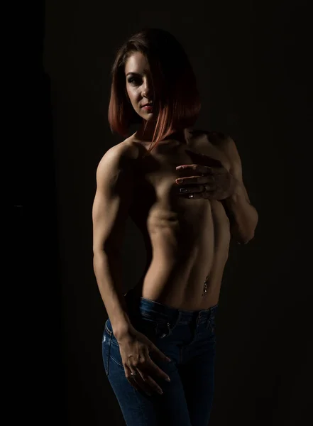 Modelo femenino joven con cuerpo muscular posa sobre un fondo oscuro — Foto de Stock
