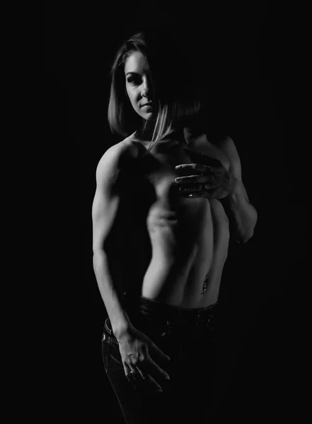 Young female model with muscular body poses on a dark background. black and white — Stock Photo, Image