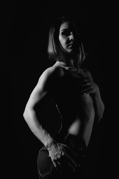 Giovane modello femminile con il corpo muscolare posa su uno sfondo scuro. bianco e nero — Foto Stock