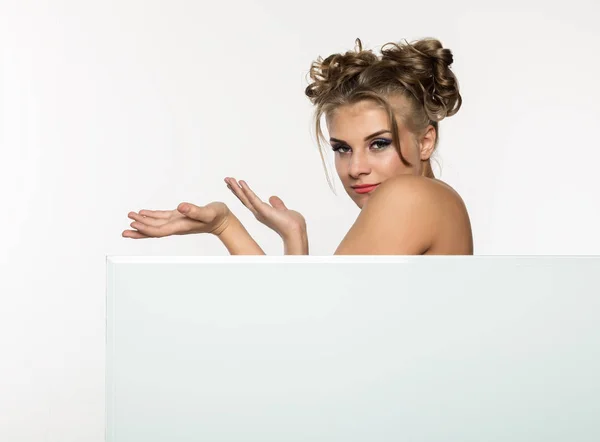 Expressive girl standing behind and leaning on a white blank billboard or placard, copy space for your text — Stock Photo, Image