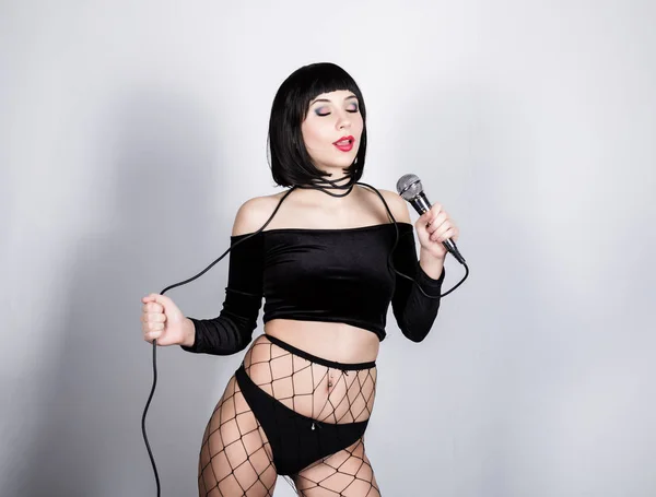 Expressive brunette woman with microphone in shorts and net stockings. — Stock Photo, Image