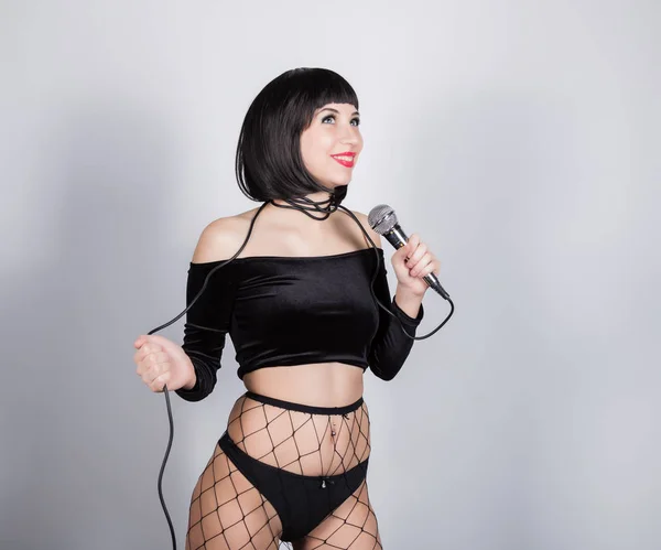 expressive brunette woman with microphone in shorts and net stockings.