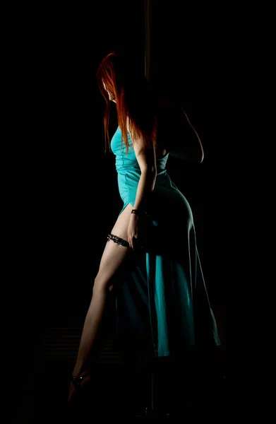 Σέξι γυναίκα χορεύτρια πόλος σε ένα μακρύ τυρκουάζ φόρεμα με ένα σκίσιμο σε σκούρο φόντο — Φωτογραφία Αρχείου
