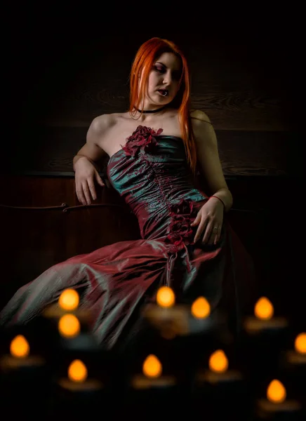 Femme rousse dans une robe rétro avec des bougies sur fond noir — Photo