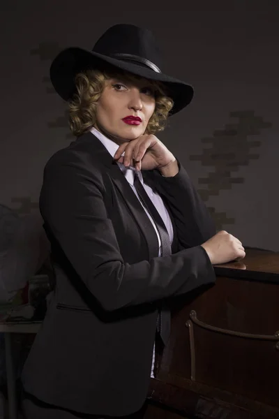 Элегантная женщина в деловом костюме в шляпе позирует на тёмном фоне, стилизованный ретро-портрет — стоковое фото