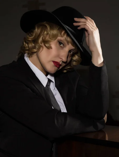 Элегантная женщина в деловом костюме в шляпе позирует на тёмном фоне, стилизованный ретро-портрет — стоковое фото