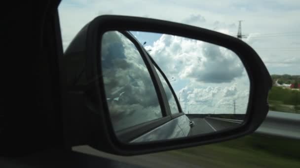 Вид бокового зеркала в машине, отражение облаков и сельской дороги через сельскую местность в летний день — стоковое видео