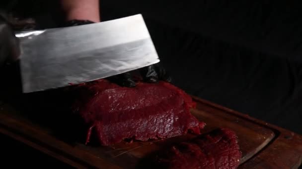 Kock skär rått kött med stor kniv på en träskiva i mörkret — Stockvideo