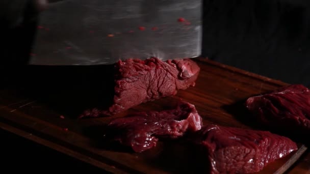 Шеф-повар режет сырое мясо большим ножом на деревянной доске в темноте — стоковое видео