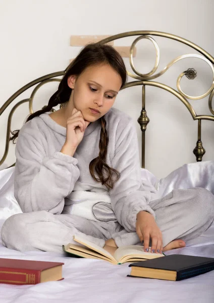 年轻的女学生在床上做作业时看书 — 图库照片