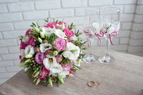 Bridal bouquet with wedding rings and  wine glasses on the table in the morning of the  day — Stock Photo, Image