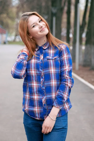 Retrato de uma menina bonita. sorrindo, posando na câmera. numa camisa azul numa jaula. No contexto do parque de outono — Fotografia de Stock