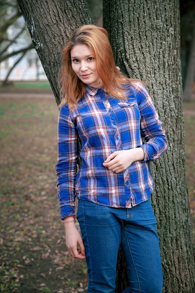 Güzel bir kız portresi. gülümseyen, kameraya poz. bir kafeste bir mavi gömlek. Sonbahar park arka planı