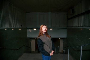 Kızıl saçlı bir kız için Altgeçit girişinde duruyor. Bir kadın dışarı metro geliyor. Işık merdivenler bakar bir adam tırmanıyor