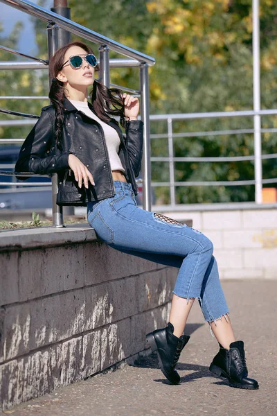 Модная молодая женщина в рок-стиле одежды, черная кожаная куртка, синие джинсы, колготки в сетке под потрепанными джинсами — стоковое фото
