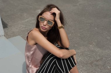 Güneş gözlüğü, ahşap bir çerçeve içinde giyen genç güzel bir moda mutlu Bayan açık portresi. Modeli giyer şık giysiler, bej bir bluz, beyaz bir şerit içinde siyah pantolon, bir çanta dolusu ışık bl