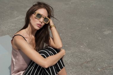 Güneş gözlüğü, ahşap bir çerçeve içinde giyen genç güzel bir moda mutlu Bayan açık portresi. Modeli giyer şık giysiler, bej bir bluz, beyaz bir şerit içinde siyah pantolon, bir çanta dolusu ışık bl