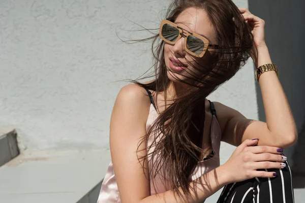 Outdoor portrait of a young beautiful fashionable happy lady, wearing sunglasses, in a wooden frame, creating a city on the street. The model wears stylish clothes. The girl is looking up. Women's fas