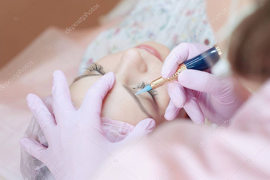 A young woman lies and gets a make-up of her eyebrows in a beauty salon. The use of permanent makeup on the eyebrows. The master works with the eyebrows. Semi-permanent makeup