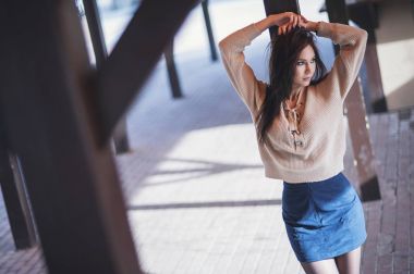 Bir örme yün bej kazaklı, ahşap durak arka plan üzerinde çekici genç bir kadın portresi. Yüz yarısı gizler ve kameraya poz veriyor