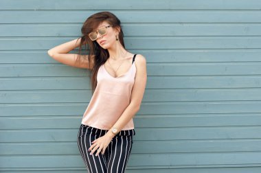 Bir gri-mavi ahşap duvar arka planda duran güzel kadın. Model beyaz bir şerit şık giysiler, bej Triko ve siyah pantolon giyer. Saç rüzgarda geliştirir. Kadın moda. U