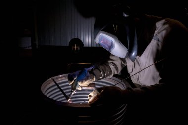 Metal ve kıvılcımlar üreten koruyucu maskeli kaynakçı.