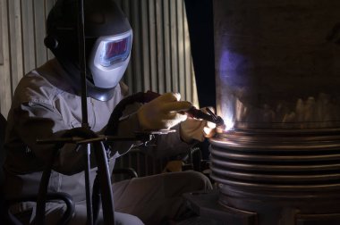 Metal ve kıvılcımlar üreten koruyucu maskeli kaynakçı.