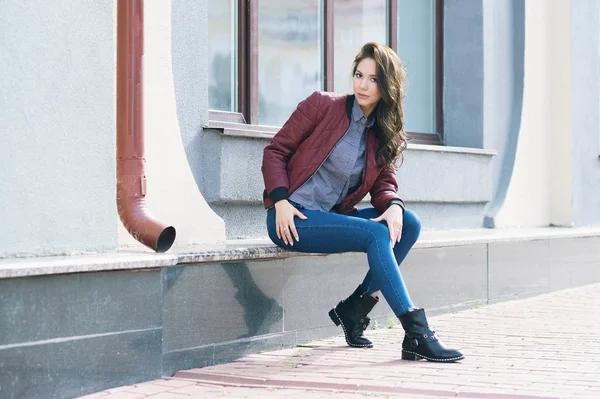 Mulher elegante bonita nova em uma jaqueta de pilotos de Borgonha e jeans azul, estilo de rua, tendência de primavera e outono, olhar, cabelo no vento — Fotografia de Stock