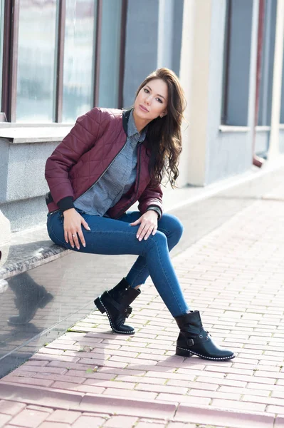 Mulher elegante bonita nova em uma jaqueta de pilotos de Borgonha e jeans azul, estilo de rua, tendência de primavera e outono, olhar, cabelo no vento — Fotografia de Stock