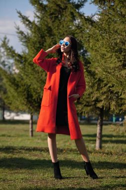 Genç güzel bir moda kadın, açık havada açık portresi. Model, bir şık turuncu ceket, güneş gözlüğü giyinmiş. Kadın moda, kentsel yaşam tarzı kavramı