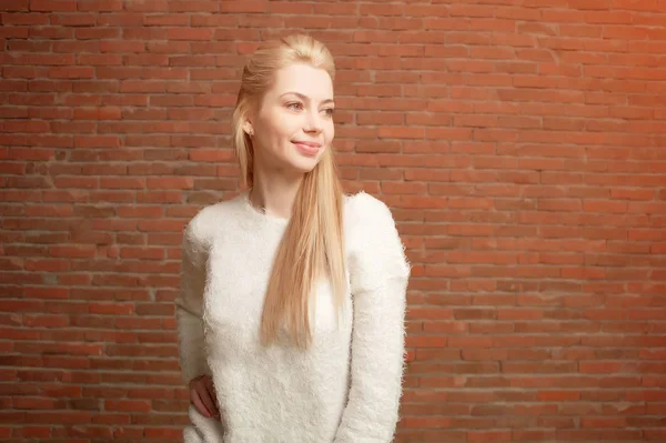 Retrato de una hermosa rubia joven con chaqueta blanca y pantalones vaqueros rojos de pie sobre un fondo de pared de ladrillo rojo —  Fotos de Stock