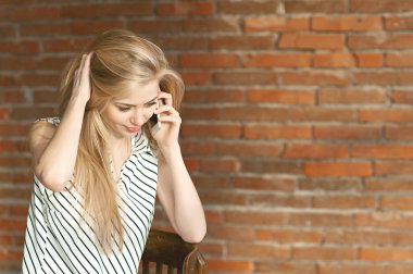 Sarışın kız daire onarım hizmetini çağırarak bir tuğla duvar arka plan, telefonla arıyor. Reklam inşaat hizmetleri