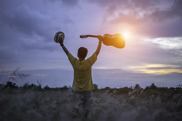 Adam gitar çayırda ile mutlu. seyahat ve günbatımı, yumuşak ve select odak — Stok fotoğraf