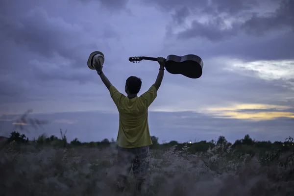 Homme heureux avec guitare dans la prairie. Voyage et coucher de soleil, mise au point douce et sélective — Photo