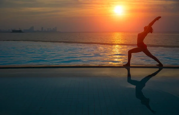 剪影年轻女子在日落时练瑜伽在海滩上 — 图库照片