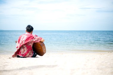 Yakışıklı adam sahilde tatil oturan klasik gitar çalmak