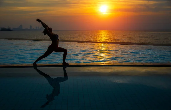 Silhouette jeune femme pratiquant le yoga sur la piscine et la plage au coucher du soleil . — Photo