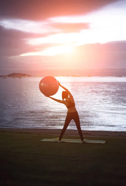 Siluet yoga topu genç kadın plaj gün batımı arka planda