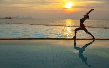 Pratik Yoga Yüzme Havuzu ve deniz üzerinde günbatımında siluet genç kadın.