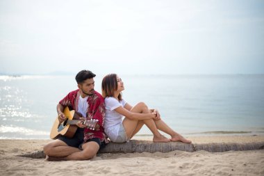 Cute hispanic couple playing guitar serenading on beach in love and embrace clipart