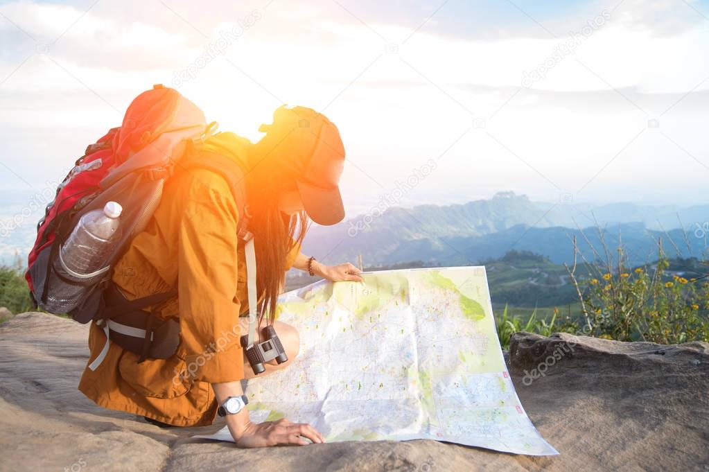 Women hiker with backpack checks map to find directions in wilderness area