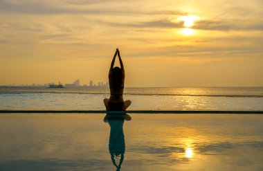 Pratik Yoga Yüzme Havuzu ve deniz üzerinde günbatımında siluet genç kadın.