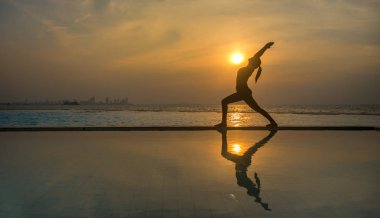 Pratik Yoga Yüzme Havuzu ve deniz üzerinde günbatımında siluet genç kadın