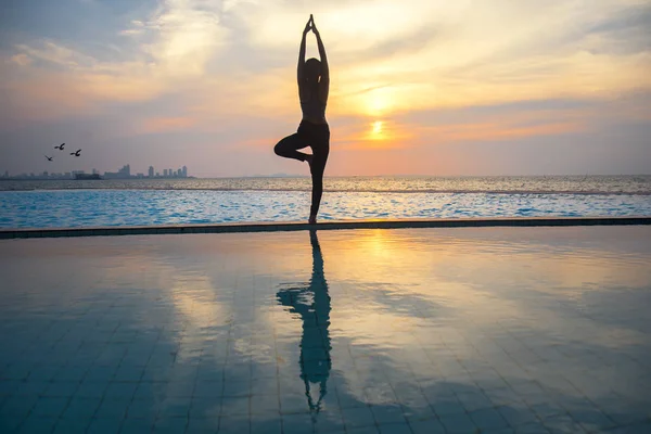 Silhouette jeune femme pratiquant le yoga sur la piscine et la plage au coucher du soleil — Photo